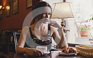 Pensive girl in sitting at the cafe going and drinking coffee with dessert.