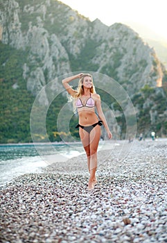 Pensive girl walking on summer sea beach in bikini