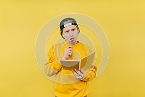Pensive guy student in headphones with a notebook isolated on a yellow background, looking at the camera with a serious face and