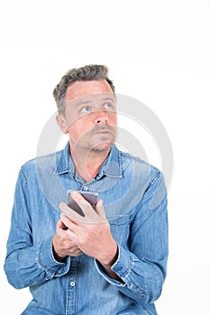 Pensive handsome man in casual blue shirt looking up aside holding phone smartphone posing isolated on white background studio