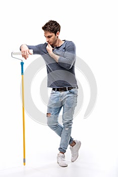 Pensive handsome man holding paint roller and isolated on white