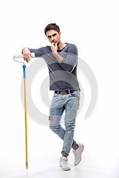 Pensive handsome man holding paint roller and isolated on white