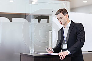 Pensive handsome speaker using mobile phone standing at tribune