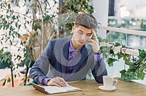 Pensive handsome young man in a business suit works at the table in coffee and holds his head with his hand