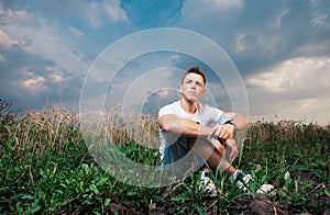 Pensive handsome young man sitting on on the green grass on a ba