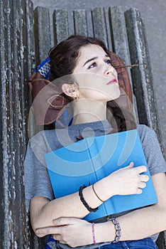 Pensive hipster girl lying on bench with blue book, adolescence lifestyl
