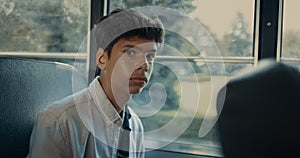 Pensive Indian boy sitting at school bus window closeup. Pupil looking camera.