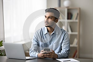 Pensive Indian man holding smartphone thinking on received message