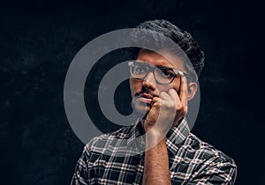 Pensive Indian student wearing eyewear and a plaid shirt.