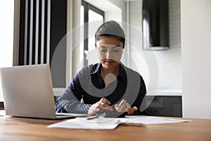 Pensive Indian woman manage finances using computer