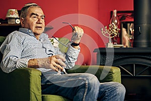 Pensive Jewish senior in the armchair drinking kosher wine