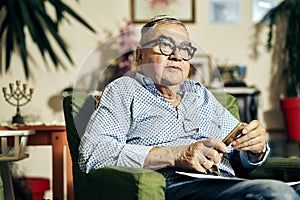 Pensive Jewish senior in the armchair reading a torah book