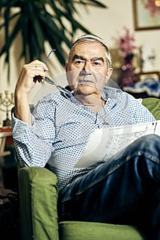 Pensive Jewish senior in the armchair reading a torah book