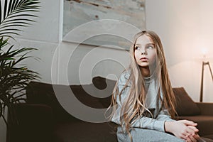 Pensive kid girl sitting on sofa alone