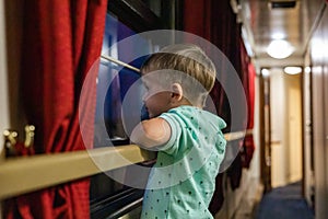 Pensive little boy looking through window traveling by train at comfortable railway carriage