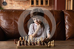 Pensive little boy play chess at home