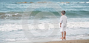 Pensive little boy standing on the beach, meditation