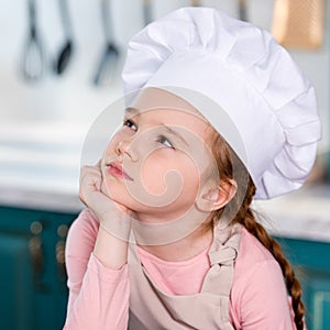 pensive little child in chef hat holding hand on chin and looking away