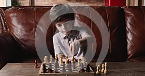 Pensive little cute boy spending time playing chess