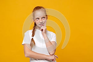 Pensive little ginger kid girl 12-13 years old in white t-shirt isolated on yellow wall background children studio