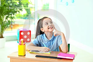 Pensive little girl doing assignment at desk in classroom