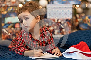 Pensive little girl writing letter to santa. kid making a wish, gift, present on new year eve. child dreaming under the christmas