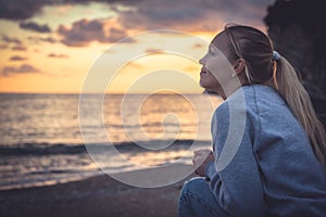 Pensive lonely smiling woman looking with hope into horizon during sunset at beach