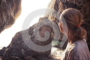 Pensive lonely woman looking with hope into horizon sunlight in rocks during sunset at beach