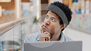 Pensive male african american guy rubbing chin thinking solution problem plan strategy startup idea sitting with laptop