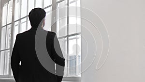 Pensive male business person in classical suit looking at windows of office building, back view