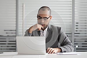 Pensive male employee look at laptop think analyzing problem