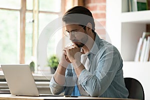 Pensive male employee work on laptop in office thinking