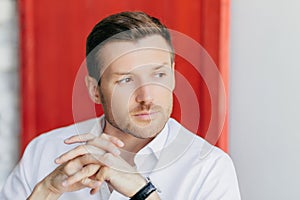 Pensive male worker, red background, deep in thoughts after meeting, owns big company