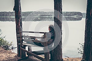 Pensive man on the high edge of river bank sitting on the bench and looking on beautiful scenery with tranquil water