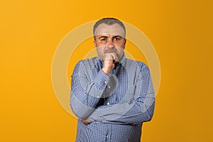 Pensive man holding hand on chin and looking at camera. Yellow background