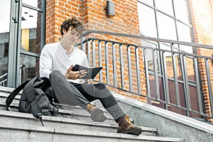 Pensive man sitting on concrete steps and making notes in his notepad.