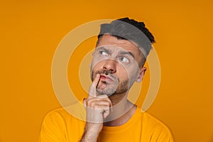 Pensive man touching his chin and looking away isolated over yellow wall