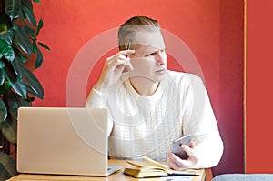 Pensive man at workplace with laptop and phone, analyzes documents, looks away. think of a new idea or project during the period o