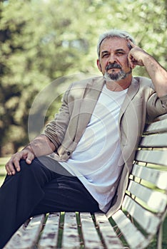 Pensive mature man sitting on bench in an urban park.