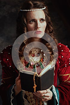 pensive medieval queen in red dress with book and rosary