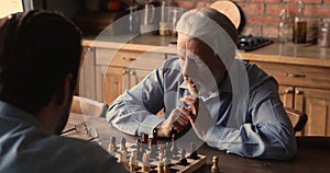 Pensive middle aged older man playing chess with grown son.