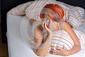 Pensive Middle Aged Redhead Woman lying in the Bed