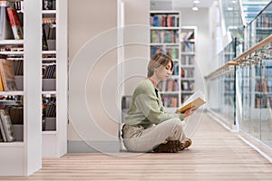 Pensive middle-aged woman with book spending free time in library, enjoying reading