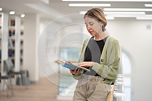 Pensive middle-aged woman literature fan with paper book in hands spending leisure time in library