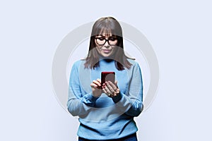 Pensive middle aged woman reading on smartphone, white background