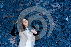 Pensive and moody young girl standing against a wall with ivy. Foliage tinted in color of the year 2020 - Classic Blue