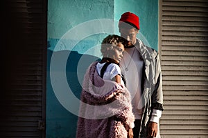 Pensive mulatto woman with trendy hairtyle and her dark skinned stylish boyfriend in red hat, stand close to each other