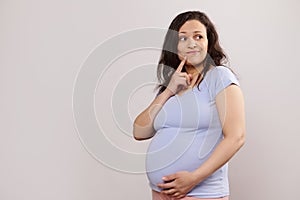 Pensive multi ethnic pregnant woman thoughtfully looking aside, gently stroking her belly, isolated on white background