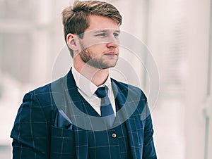 Pensive newcomer businessman in a business suit stands near a wi