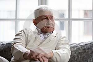 Pensive old man sitting on couch in living room alone photo